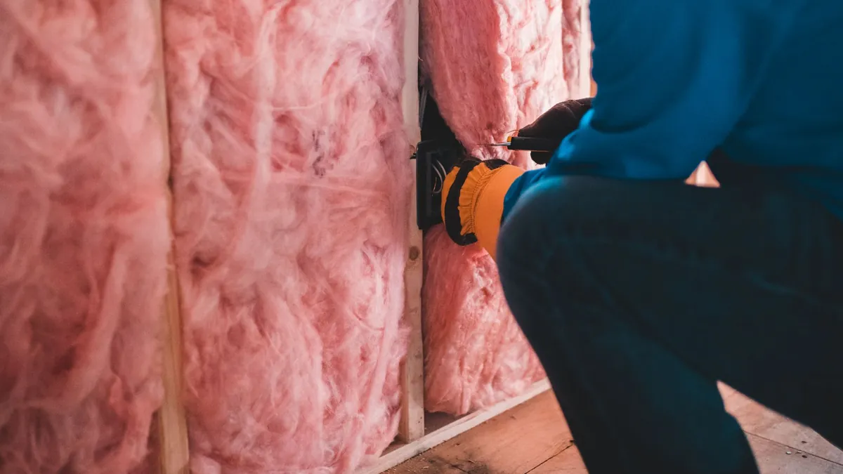 An installer fitting fiberglass batt insulation into a wall cavity